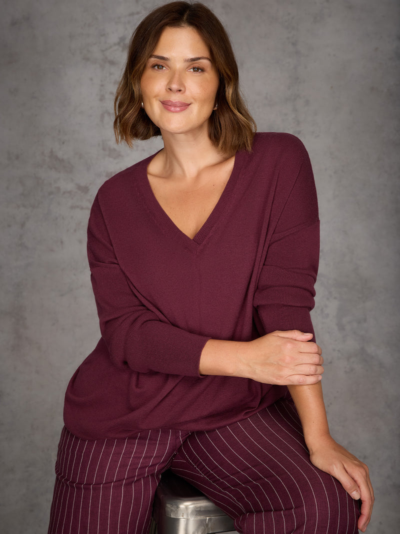 Woman wearing a burgundy top and striped pants against a gray background