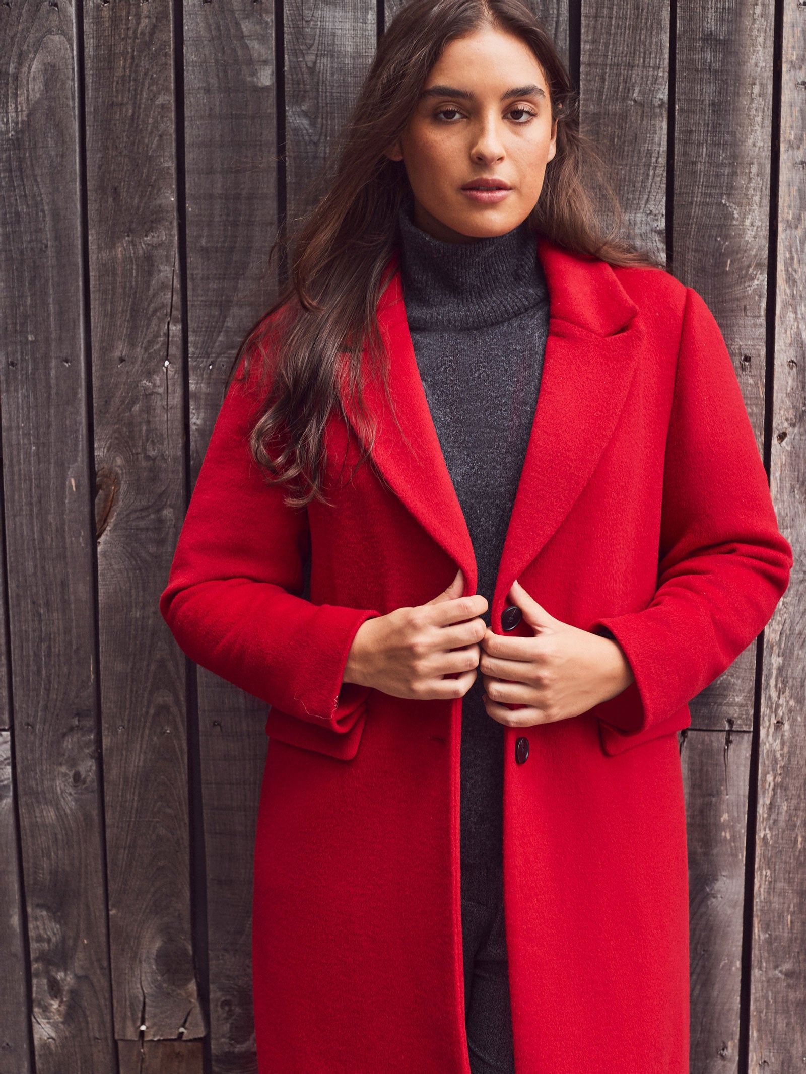 Woman wearing a red coat standing against a wooden wall