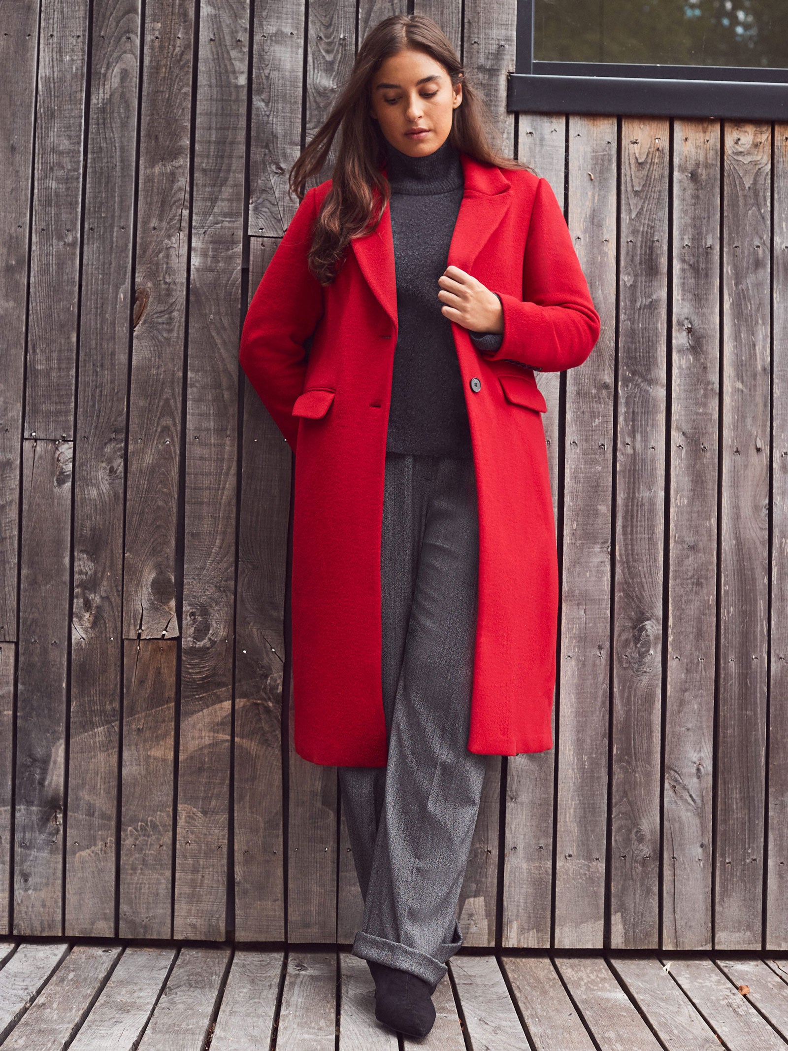 Woman wearing a red coat standing against a wooden wall.