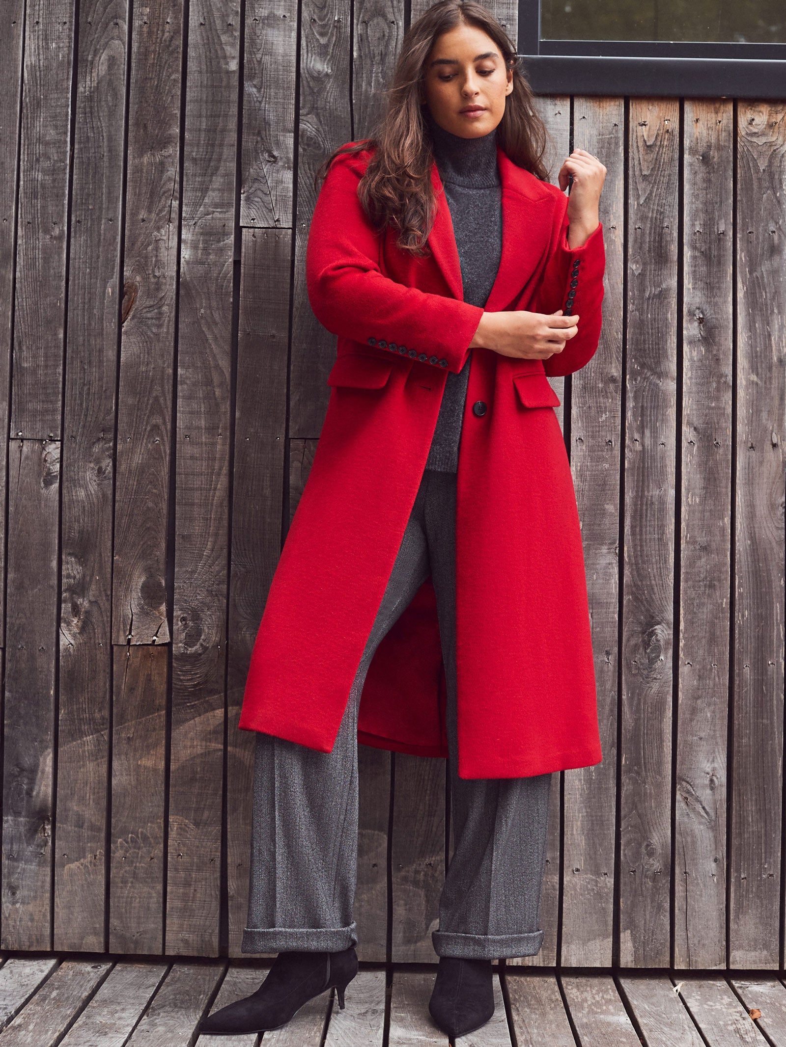 Woman wearing a red coat standing against a wooden wall.