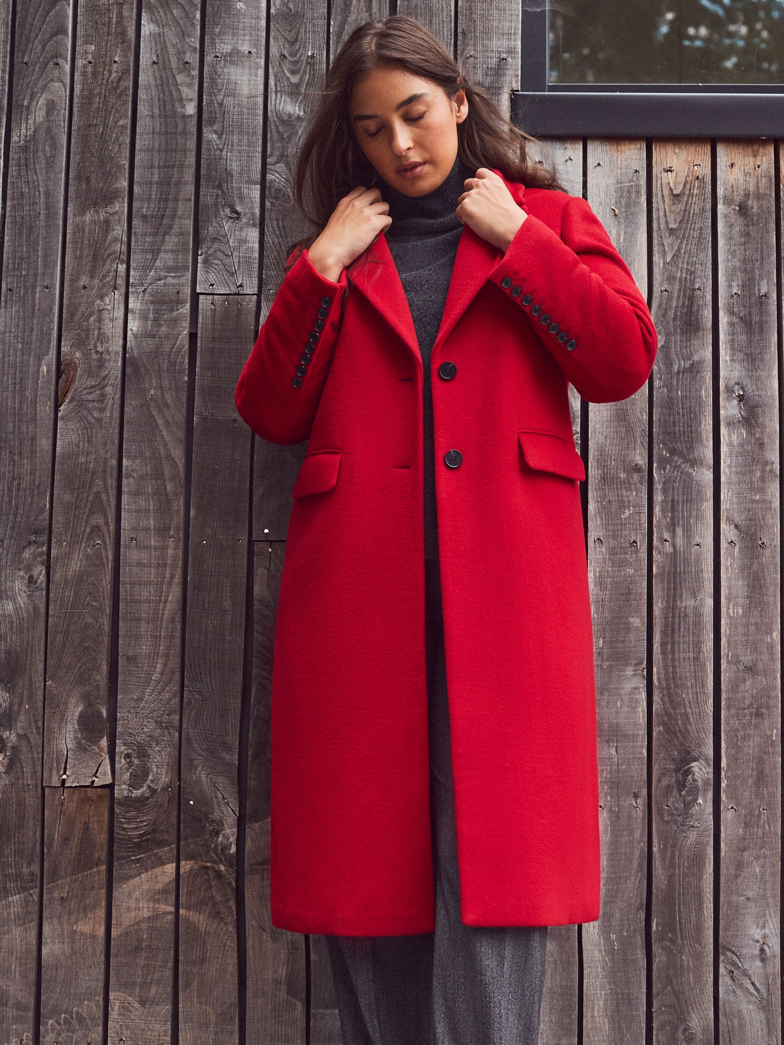 Woman wearing a red coat standing against a wooden wall
