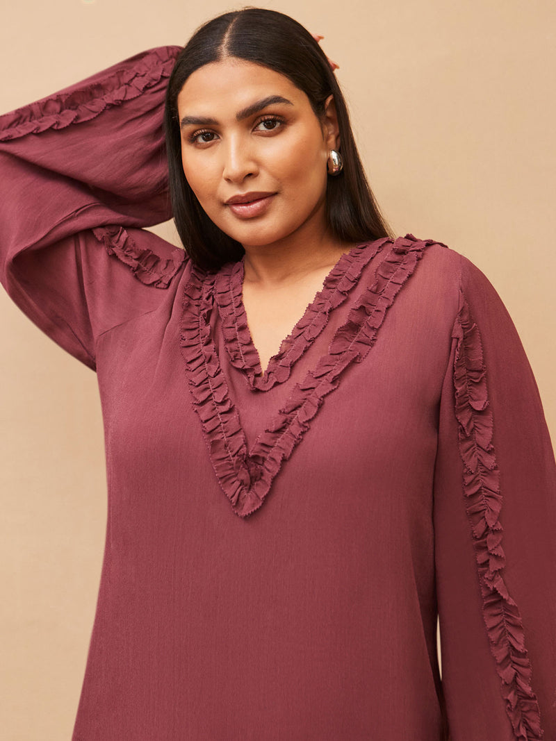 Woman wearing a burgundy dress with ruffled details against a beige background