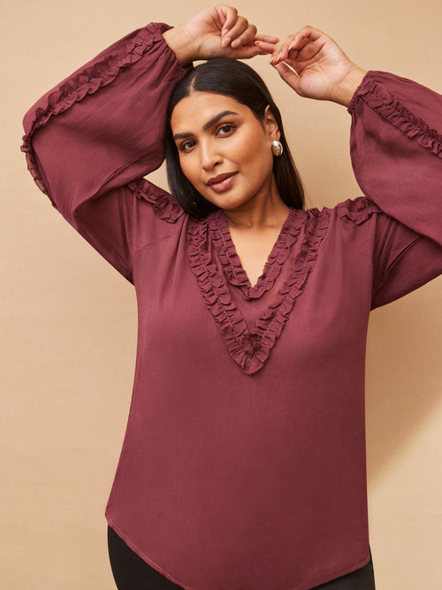 Woman wearing a burgundy blouse with ruffled details on a beige background