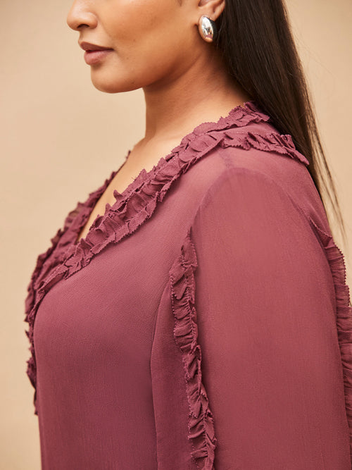 Close-up of a person wearing a burgundy top with ruffled details on a beige background