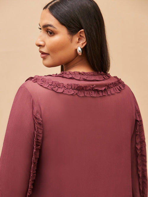 Woman wearing a burgundy blouse with ruffled details on a beige background