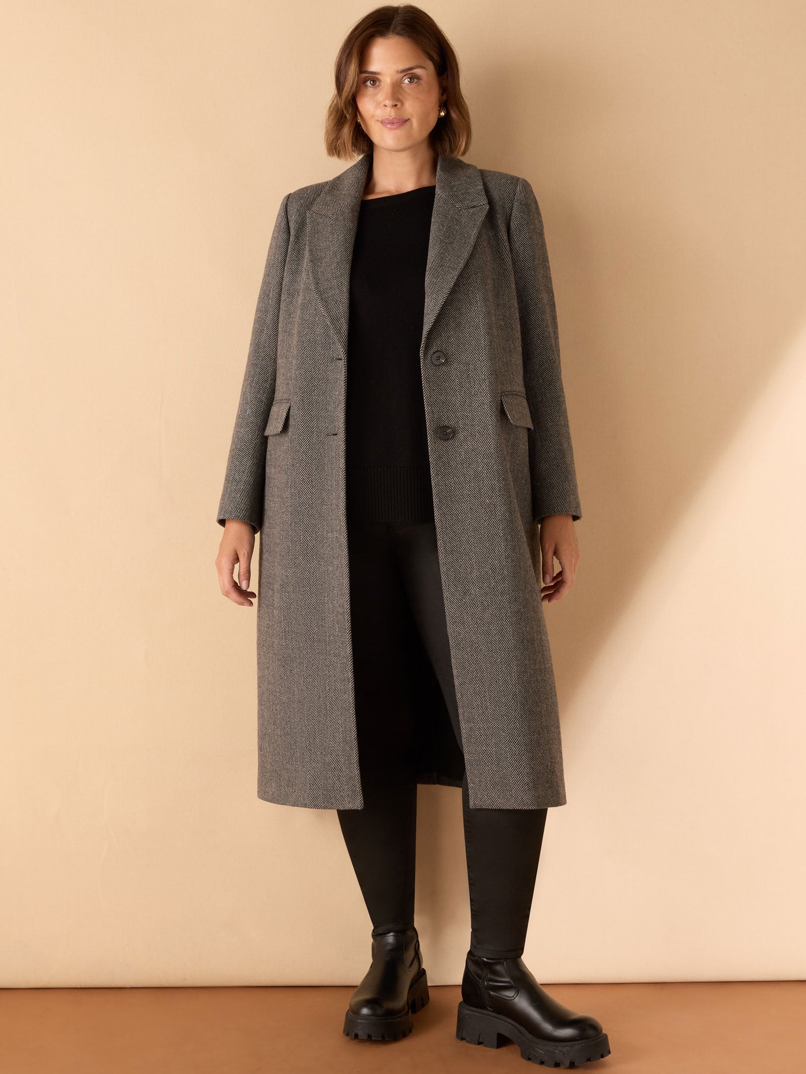 Woman wearing a gray coat over a black outfit on a beige background