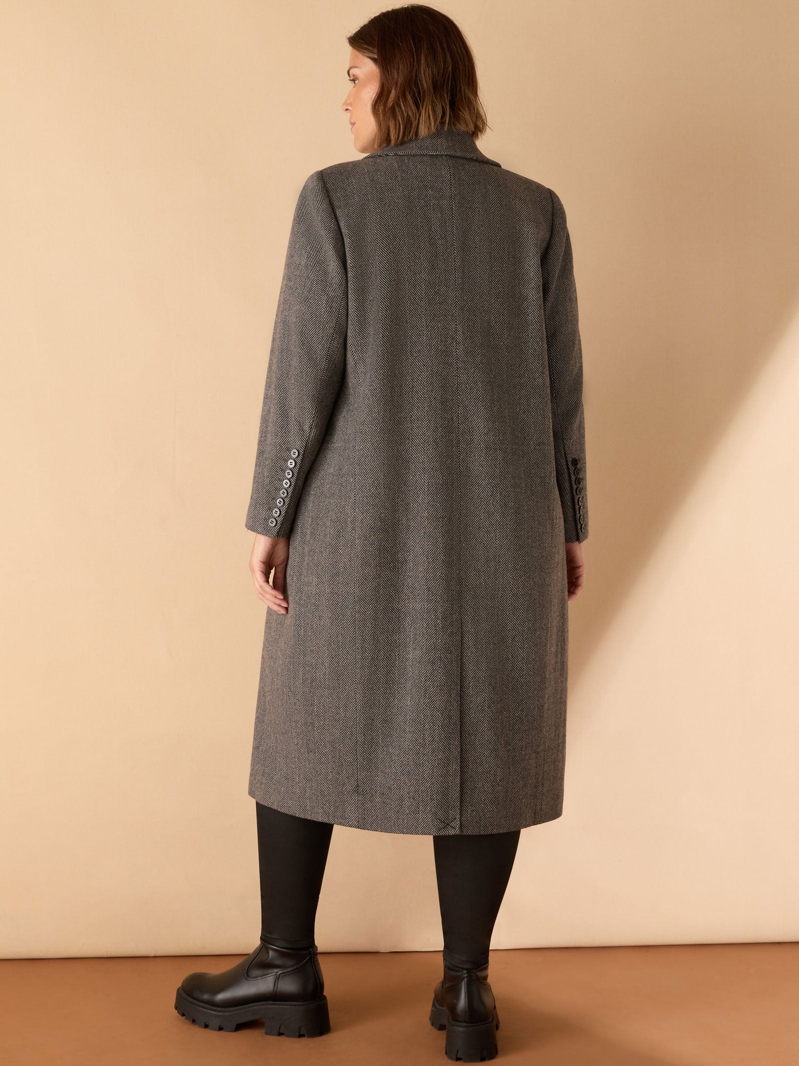 Person wearing a gray coat standing against a beige background