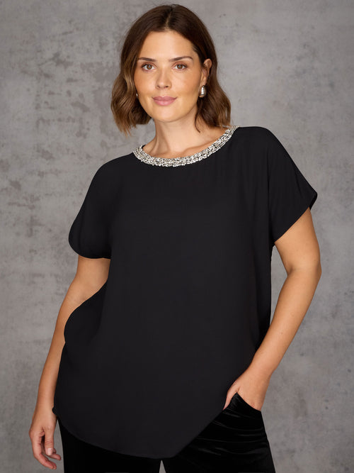 Woman wearing a black top with a decorative neckline against a gray background