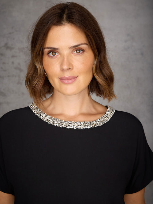 Woman wearing a black top with a silver neckline against a gray background