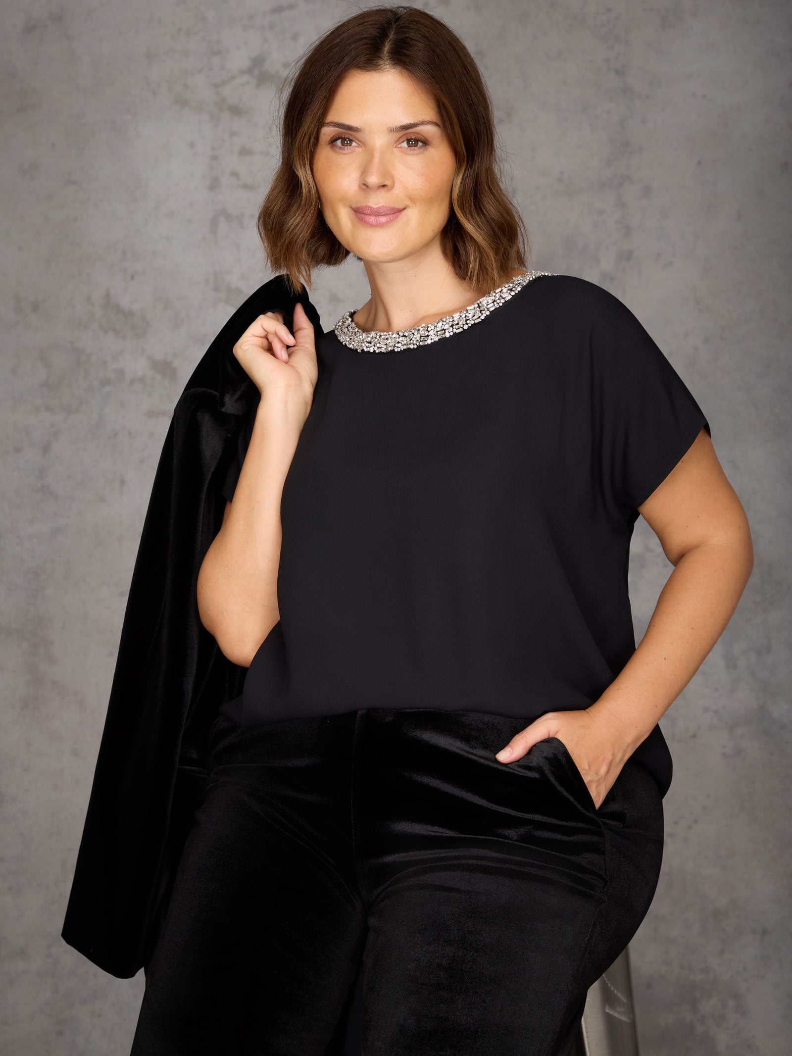 Woman wearing a black outfit with a textured collar against a gray background