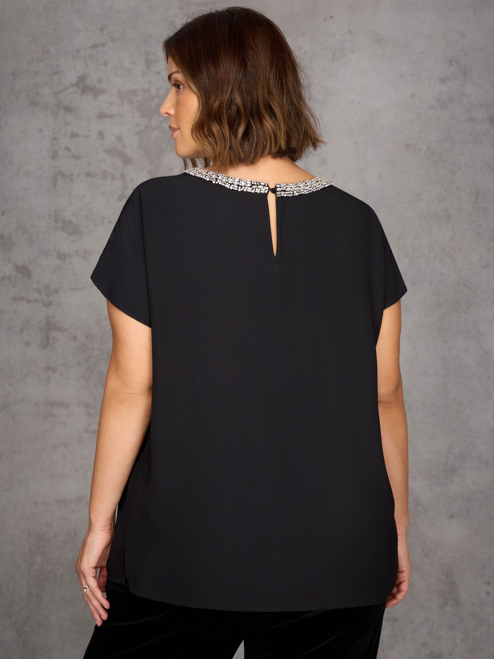 Woman wearing a black top with a decorative back detail against a gray background