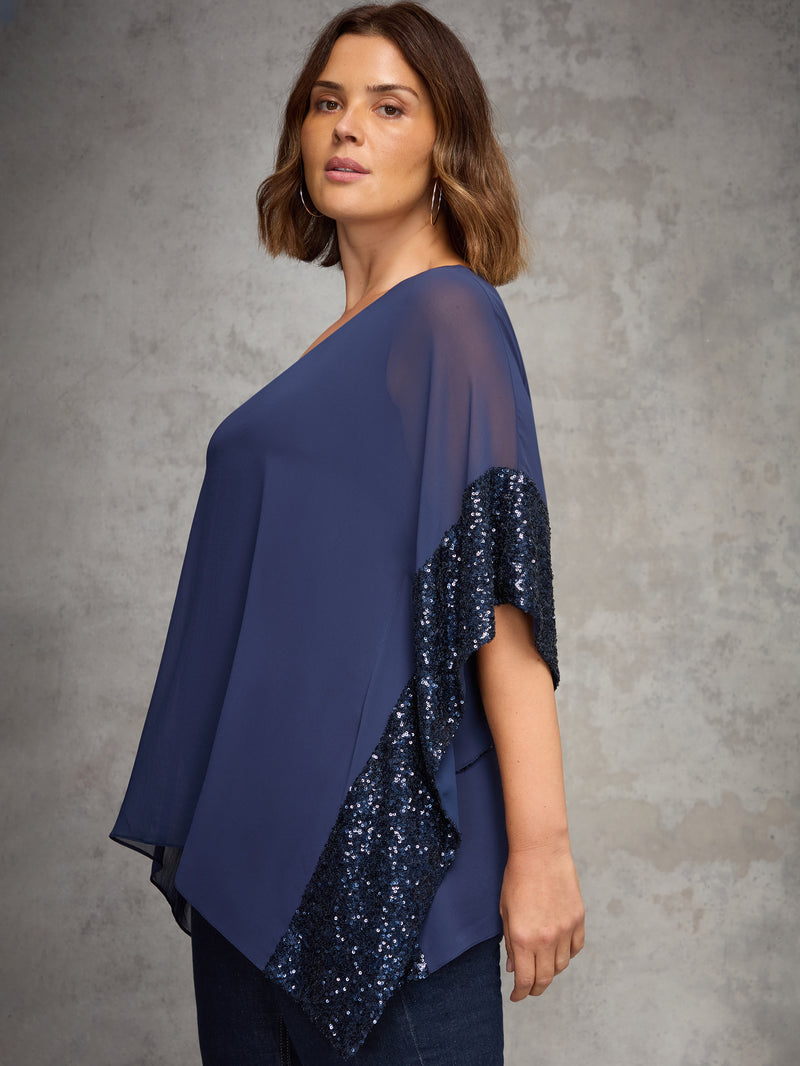 Woman wearing a blue top with sequin details on a gray background