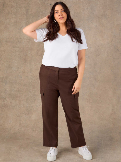 Woman wearing a white t-shirt and brown cargo pants against a beige background