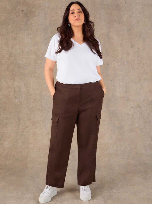 Woman wearing a white t-shirt and brown cargo pants against a beige background