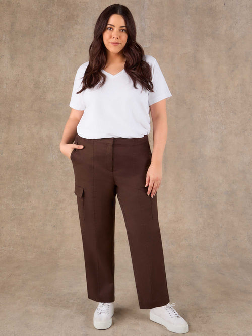 Woman wearing a white t-shirt and brown cargo pants against a beige background