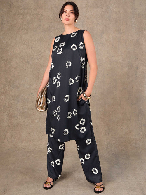 Woman wearing a black sleeveless top and pants with white floral patterns against a brown background