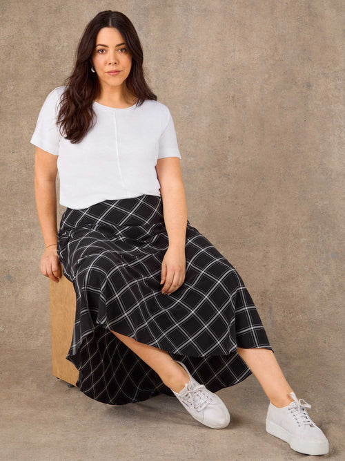 Woman wearing a white top and black checkered skirt sitting on a brown chair against a brown background