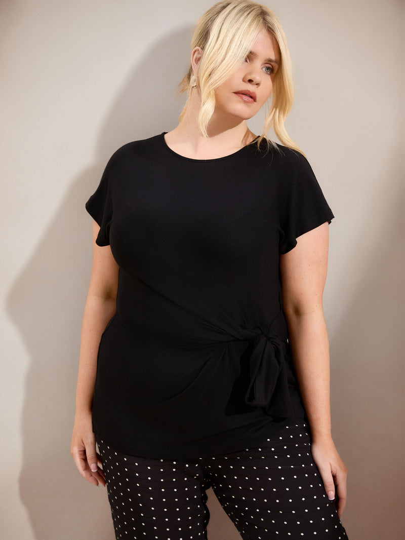 Plus size black jersey top with contrast neckline, cap sleeves and side tie detail, ideal for casual and smart-casual outfits.